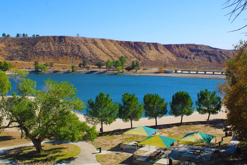 A view of a recreational area in front of a bright blue Castaic Lake in LA County with arid flat hills in the background.